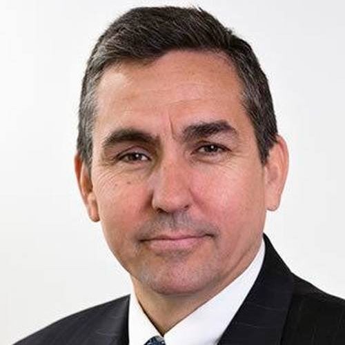 Man in a suit with short dark hair and a neutral expression against a plain background.