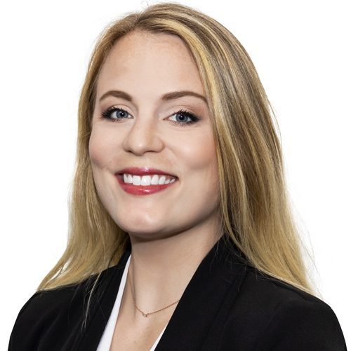 Smiling woman with long blonde hair, wearing a black blazer and white top, against a white background.