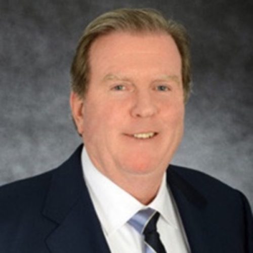 Smiling man in a suit and tie against a dark, textured background.