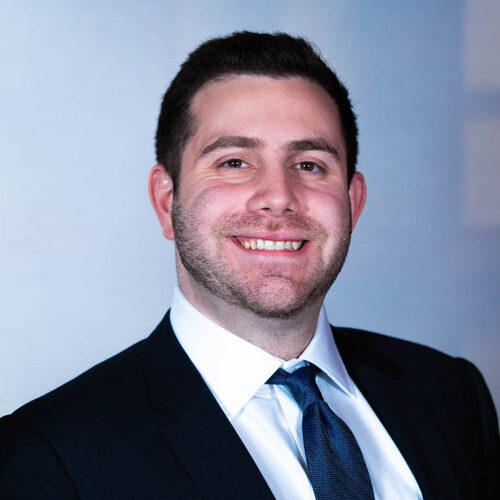 Smiling man in a suit and tie against a neutral background.